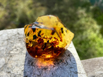 Transparent amber stone on a textured surface with blurred greenery in the background