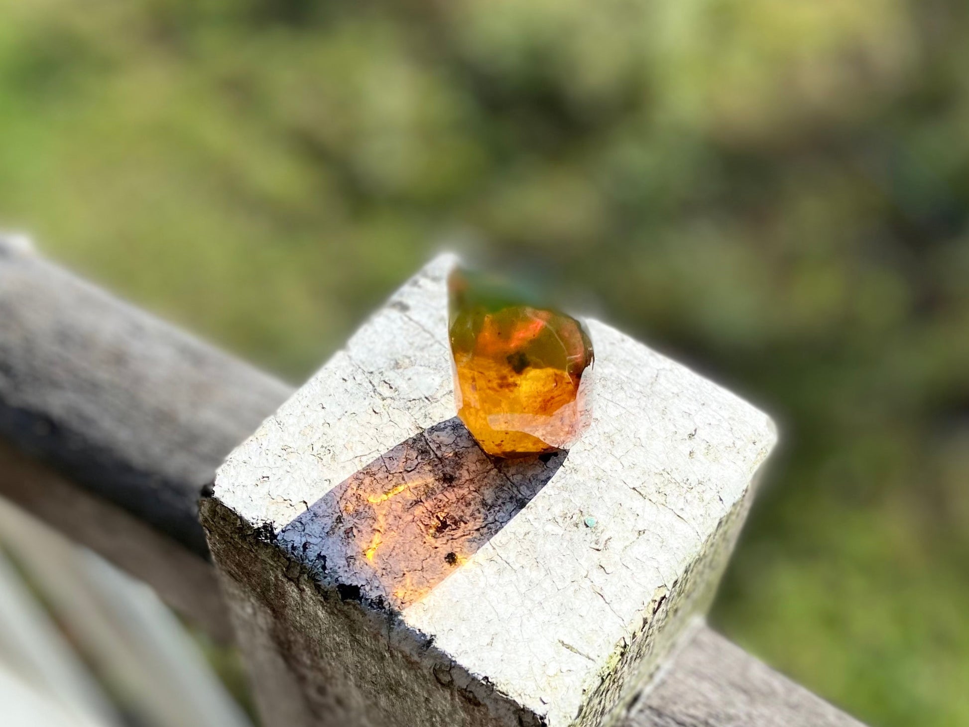 Crystal with a yellowish-orange stone on a wooden surface with a blurred natural background